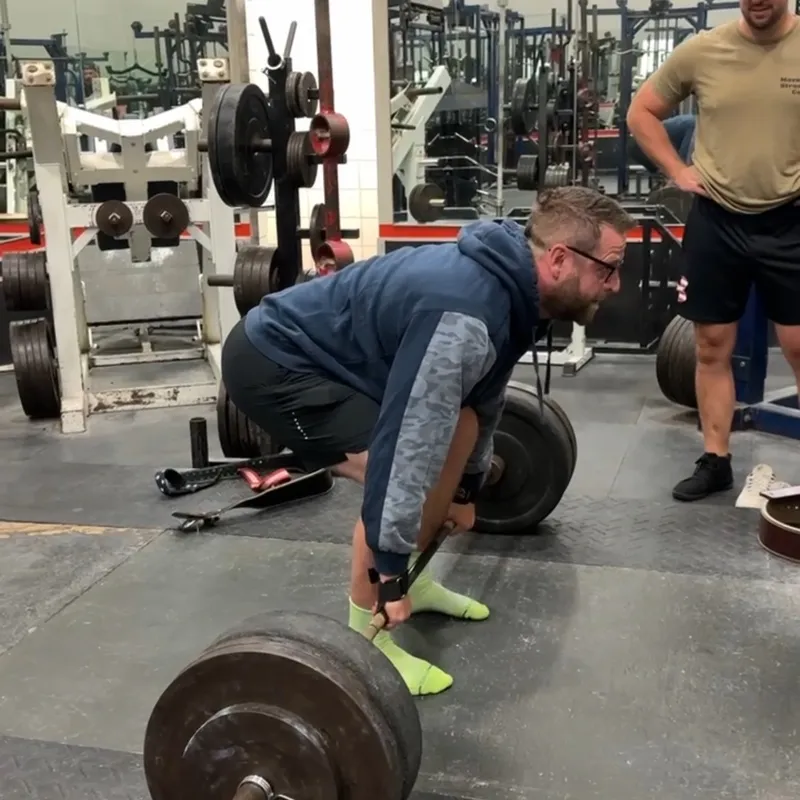 Athlete performing heavy deadlift with coach observing in professional gym